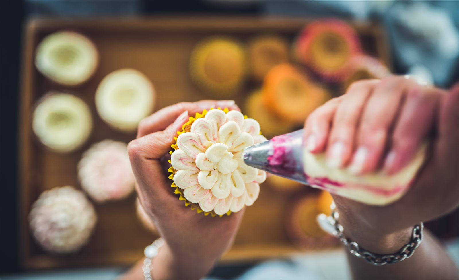 A baker piping a colourful buttercream flower onto a cupcake with an Eazy piping bag